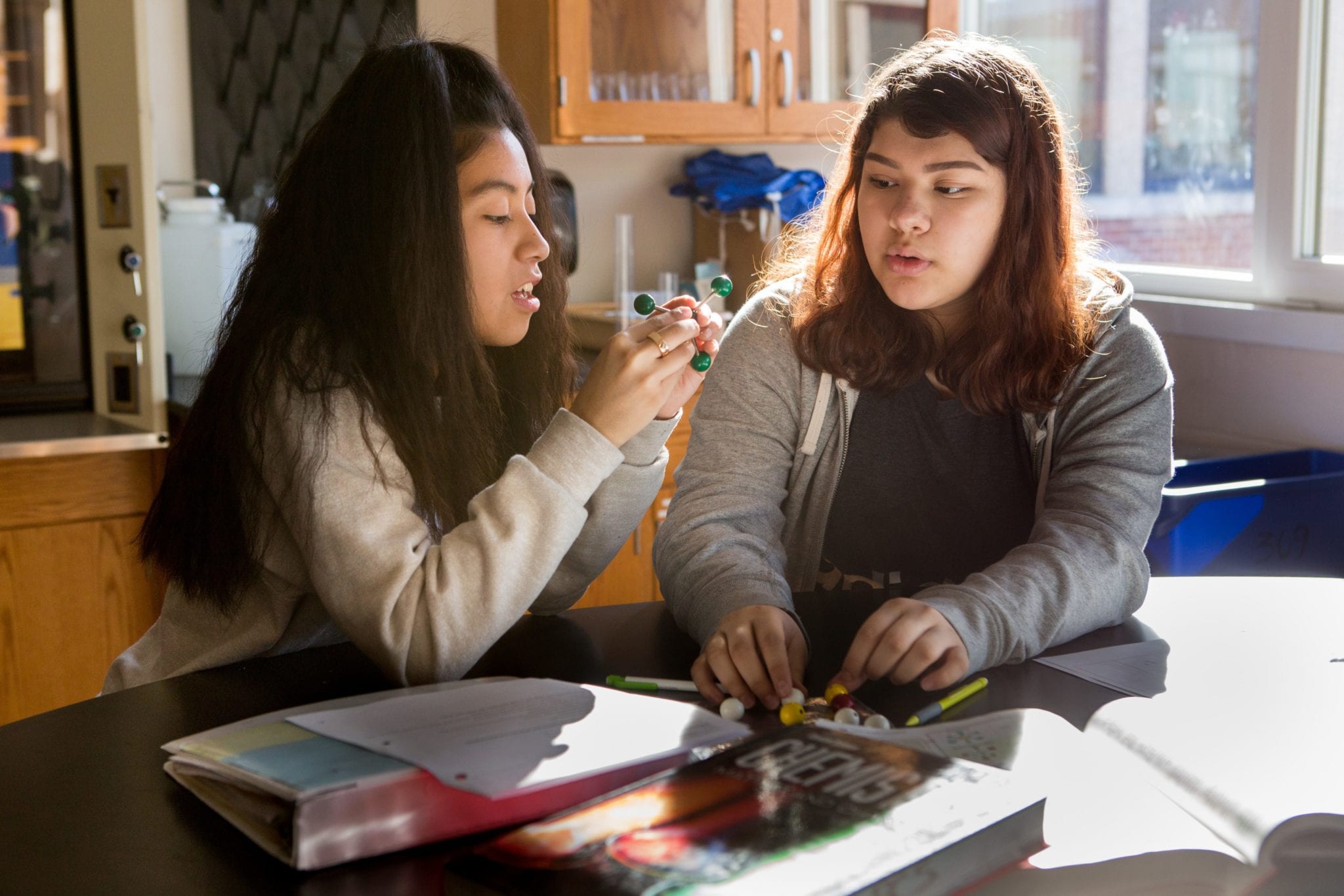 Two female students in a high school chemistry classroom working on a 3-D model