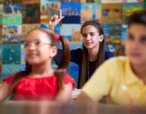 Young female student raising her hand in classroom