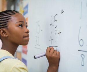 A young, female student solving a math equation on a whiteboard