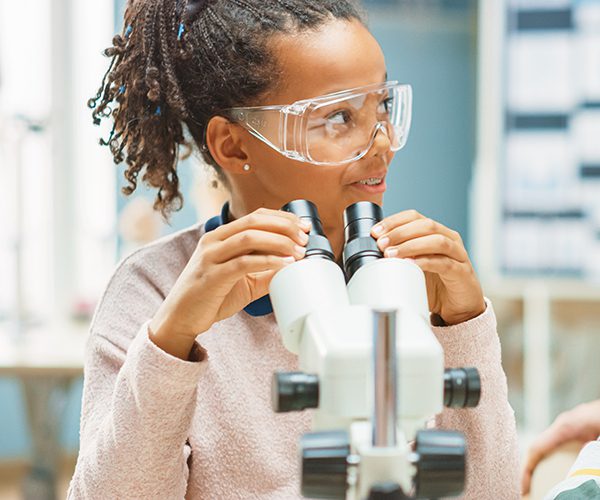 Black girl wearing goggles looking at a microscope