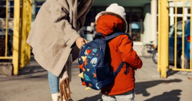 Kindergarten student with backpack being led into school by female adult