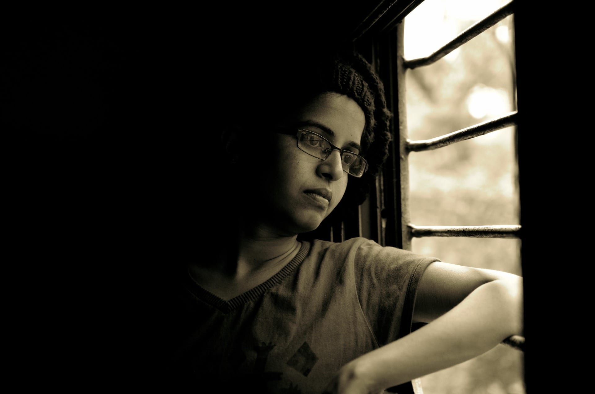 Young boy looks outside of window with gloomy look on face