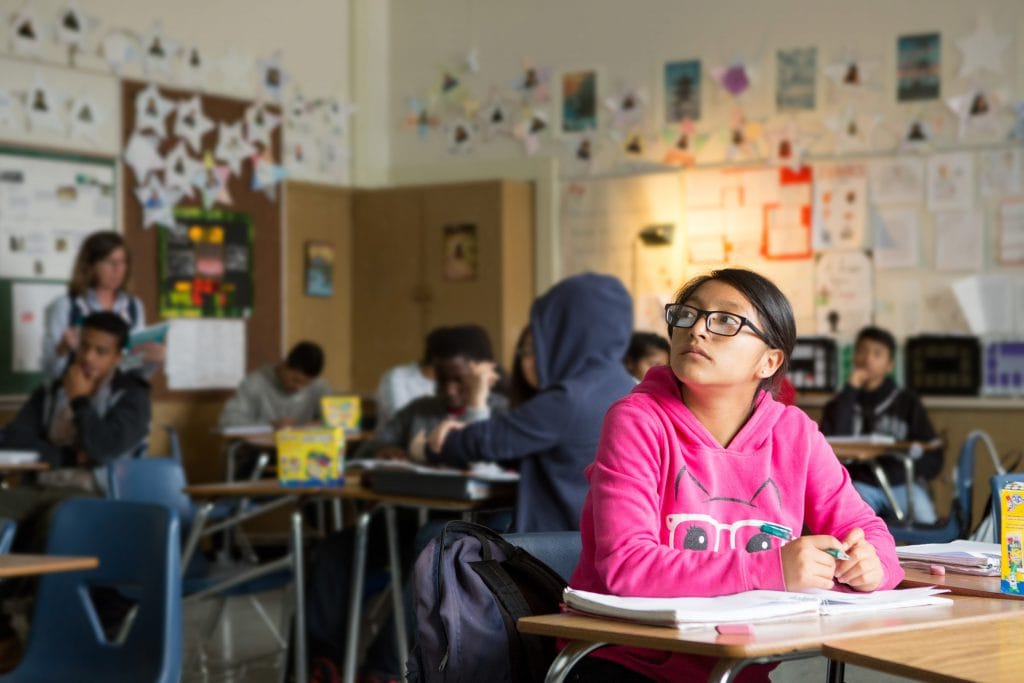 A female student in the foreground with her classmates in the background in a classroom