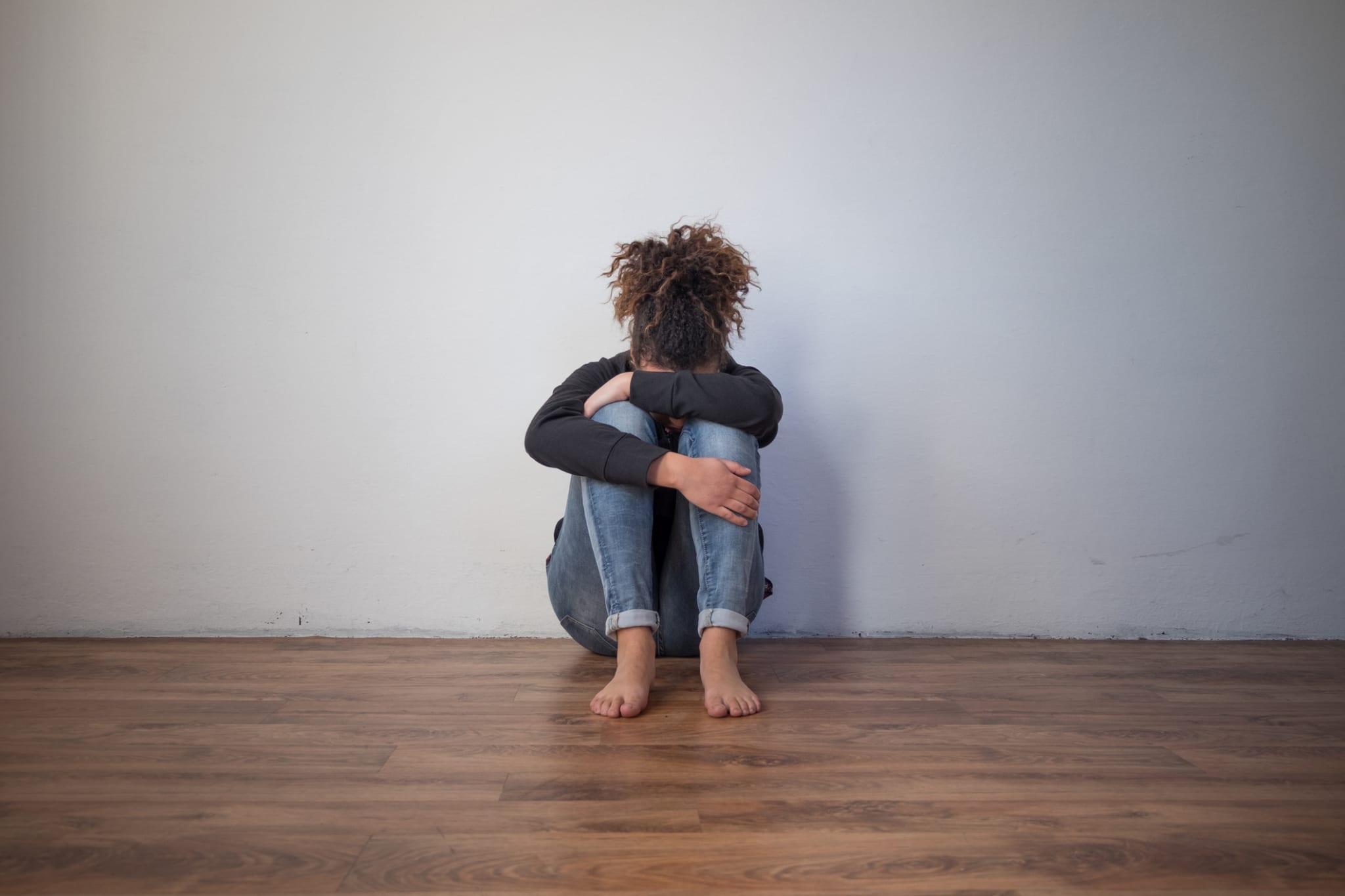 Sad black girl sitting alone on the floor, hugging her knees