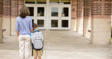 Black boy clings to his mom as they walk into school building