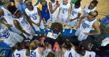 Coach discusses plays in a huddle with female basketball players
