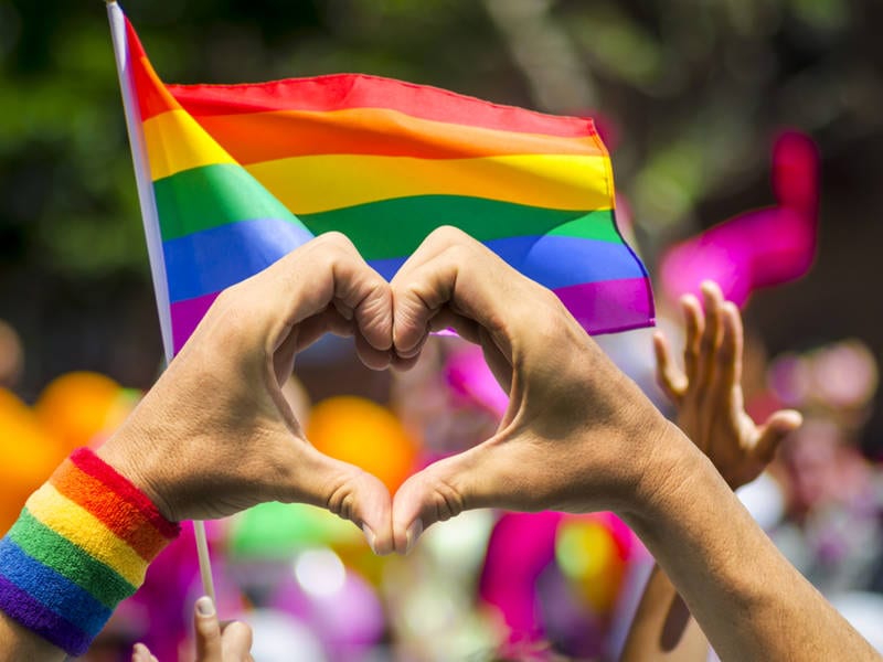 Two individuals forming heart with hands in front of pride flag