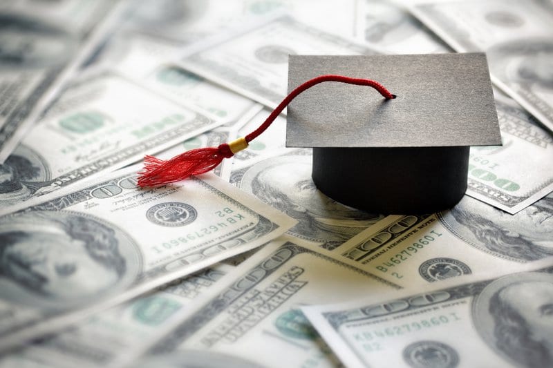 A graduation cap on top of one hundred dollar bills