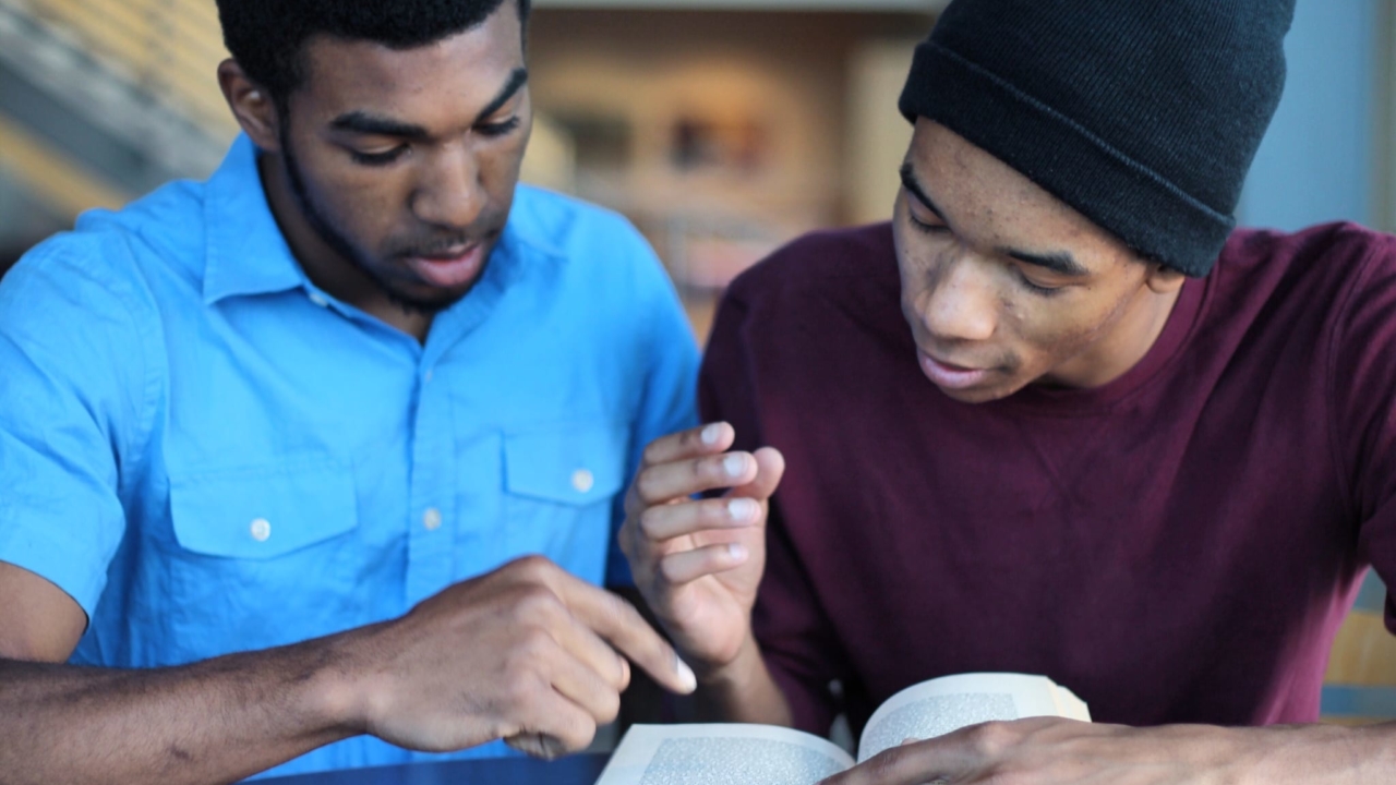 Two male students reading a book together