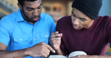 Two male students reading a book together