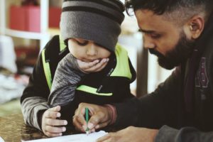 A man and a toddler drawing on paper