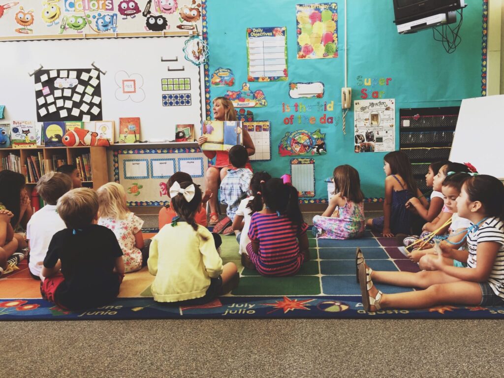 Kindergarten students sitting on the floor listening to their teacher in a classroom