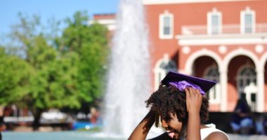 Black girl wearing graduation cap in front of fountain and building
