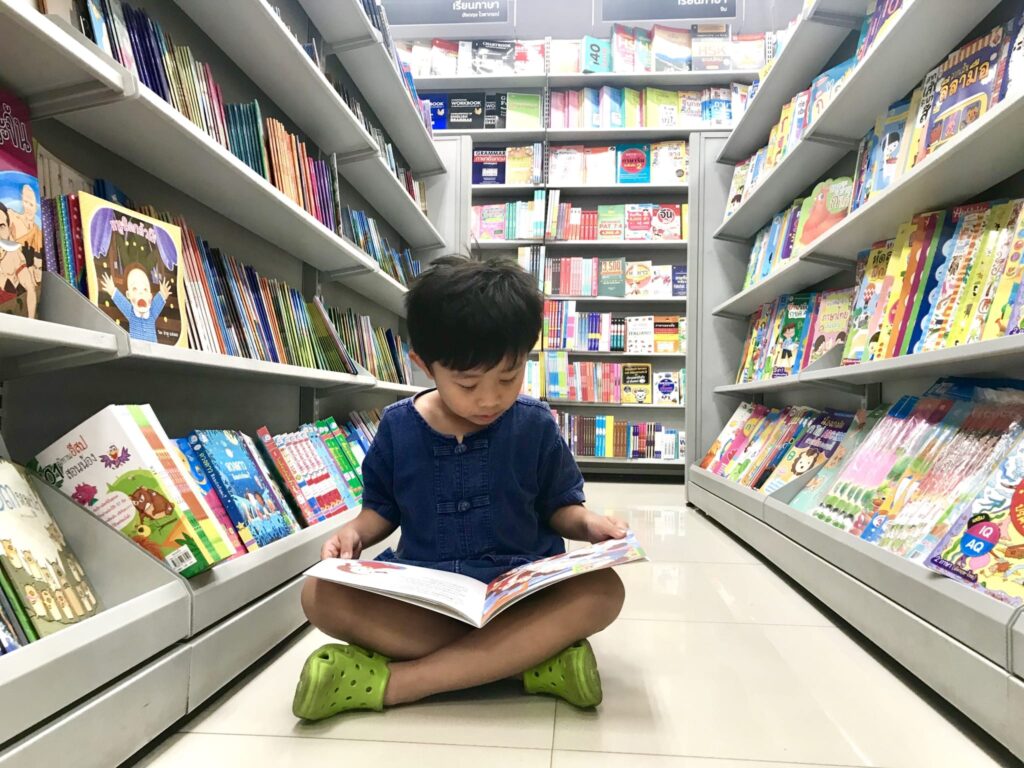 Male child sitting Indian style in library aisle and reading a book