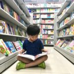 Male child sitting Indian style in library aisle and reading a book