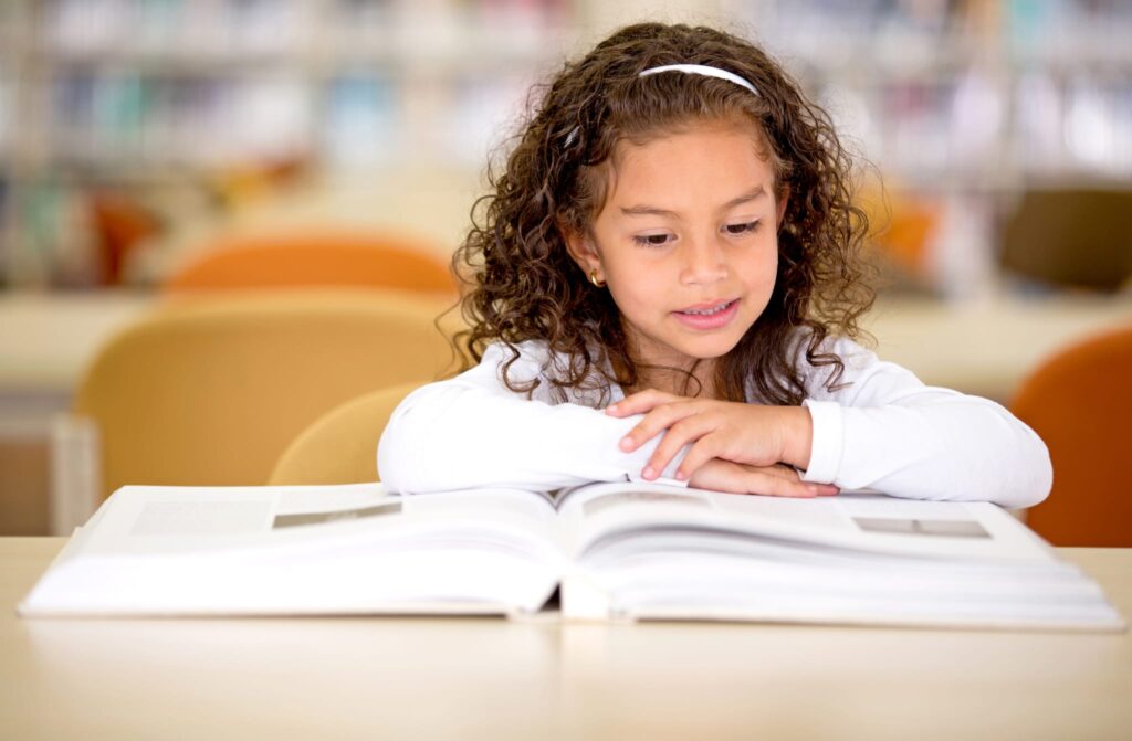 Young girl reading a book at a table in a library