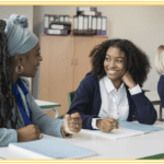 Black female teacher talking with black female teenage student at a desk
