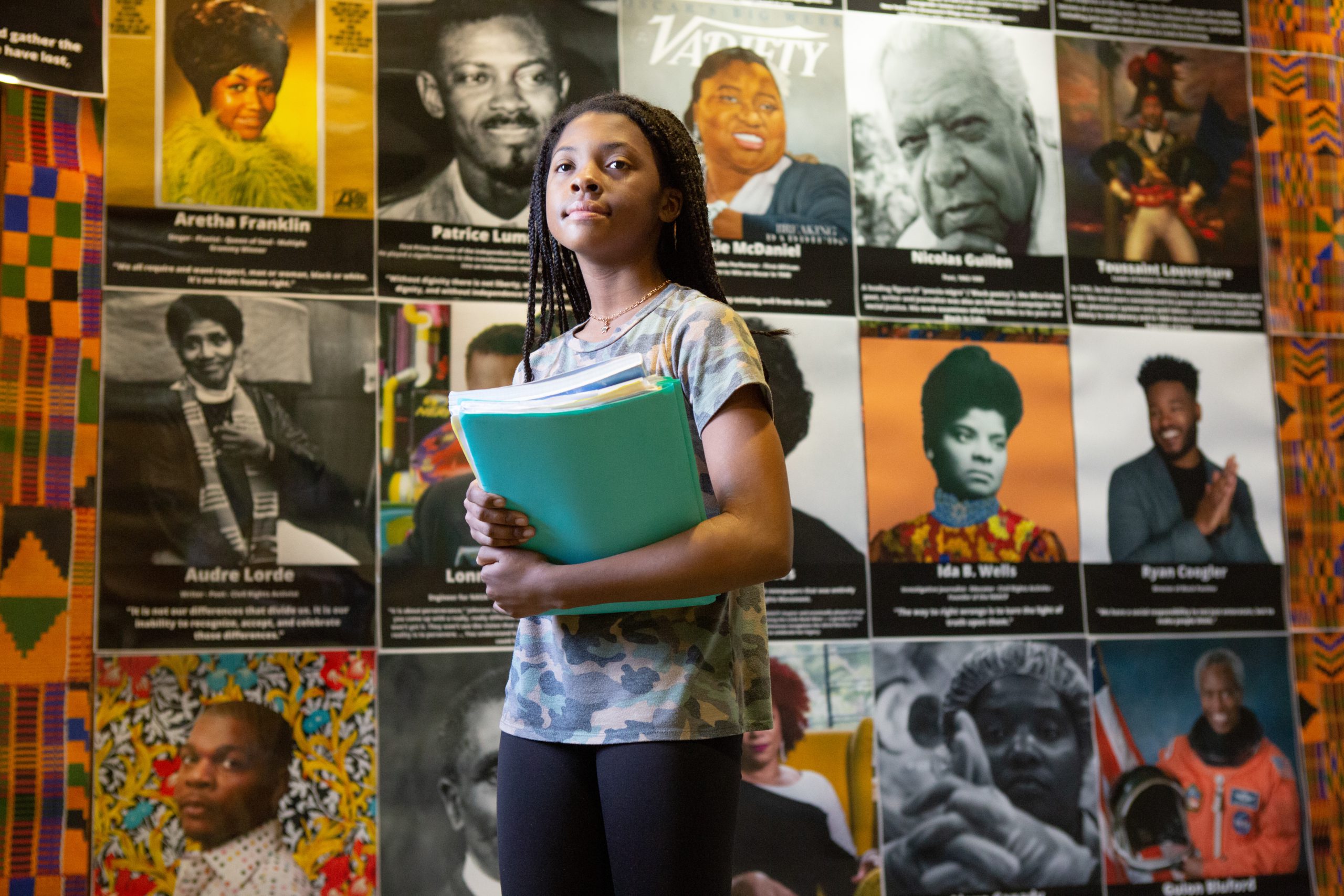 Black female student holding books in front of posters of African Americans