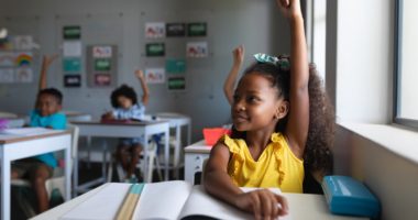 young black student raising her hand in a classroom