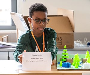 A young male black student sitting at a table with his science project