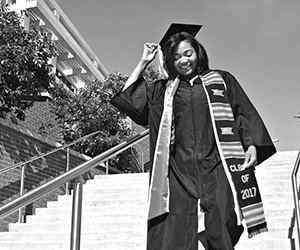 Black female graduate in cap and gown walking down stairs