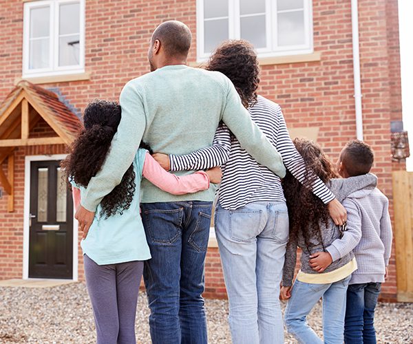 Back view of a black family embracing each other in front of a house
