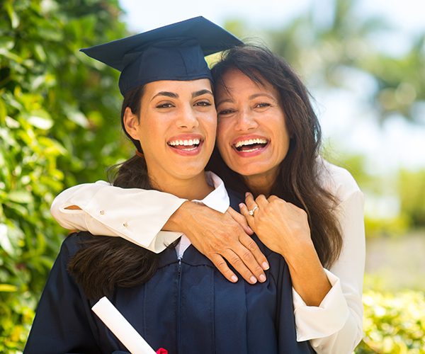 Female graduate in cap and gown embraced by older female