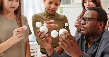 A black male teacher demonstrating a model of planets to three, multiracial female students
