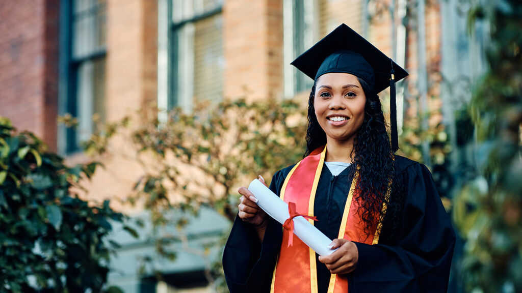 Black female college graduate wearing a graduation toga and cap and holding a diploma