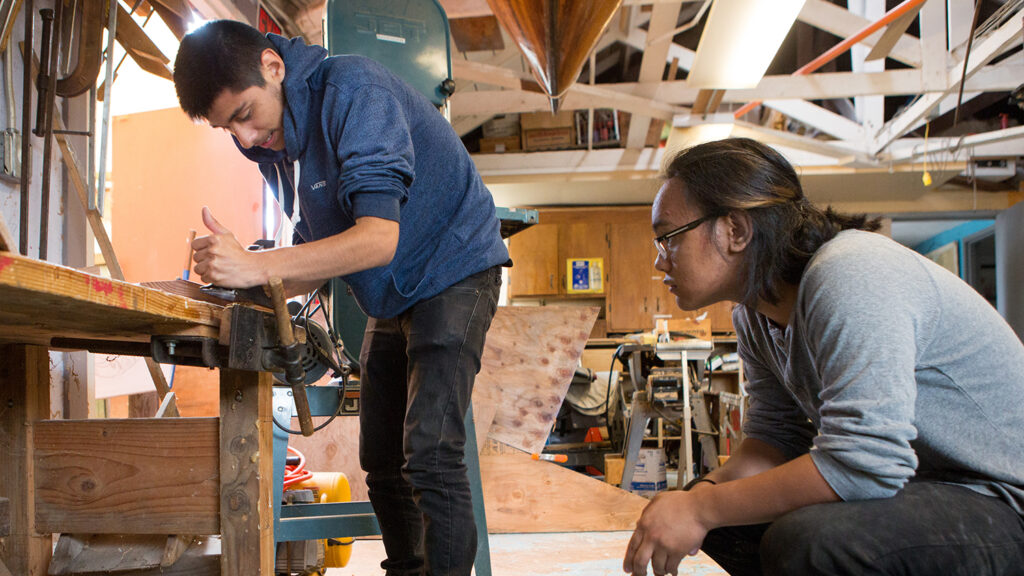 A student fabricates parts of a solar-powered boat while an instructor supervises.