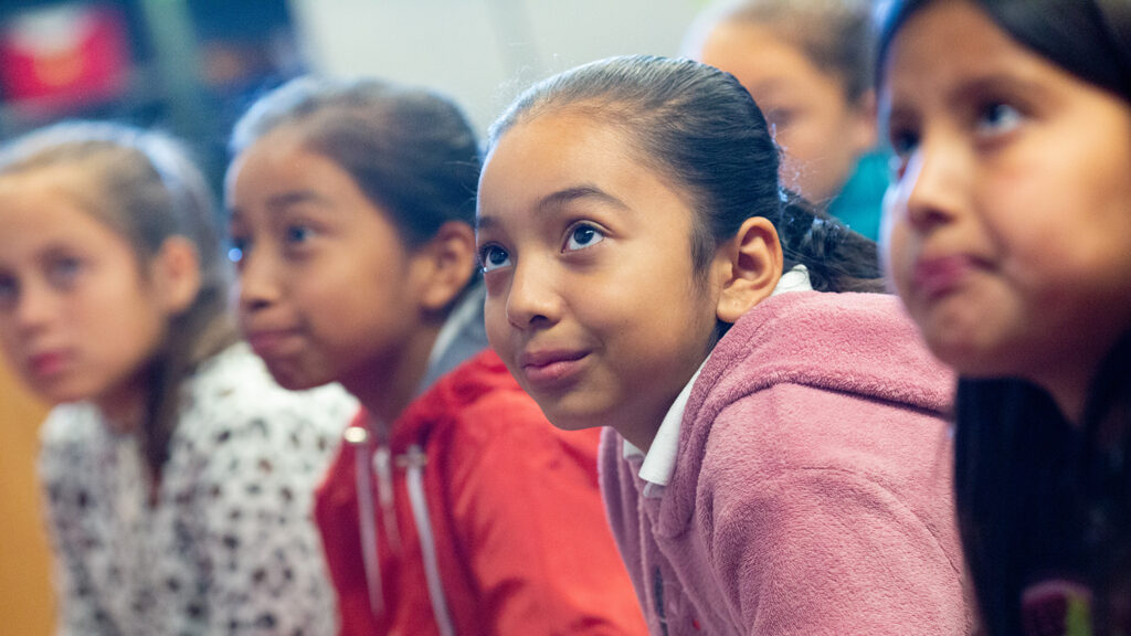 A group of elementary school girls listens to their teacher during class.