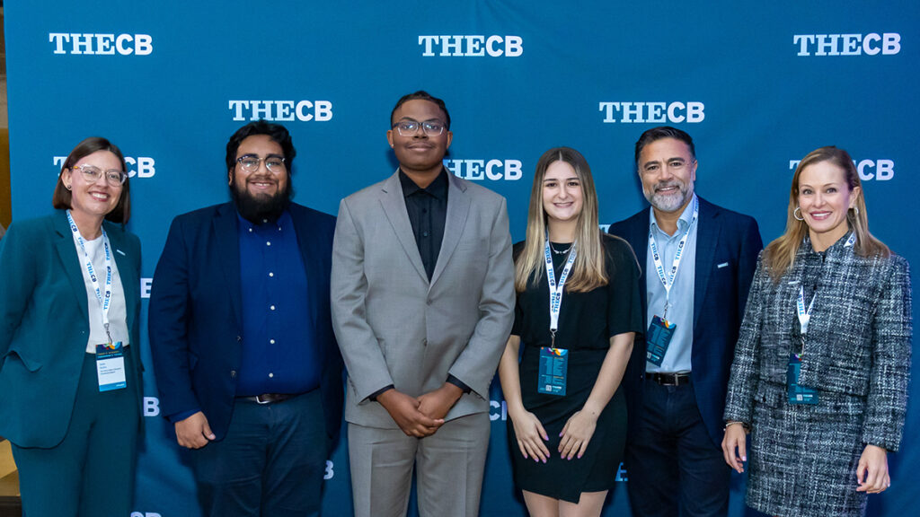 A multiethnic group of six people posing in front of a banner with TheCB logo on it