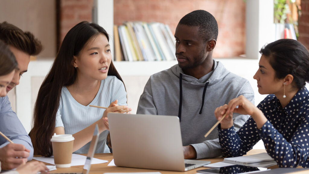 College students discussing their work around a table with a laptop open in front of them