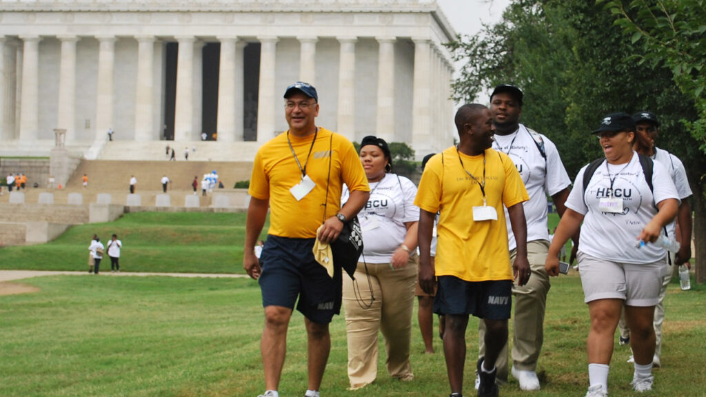 A group of black college students led by a middle-aged black man walking with the Lincoln Memorial in the background