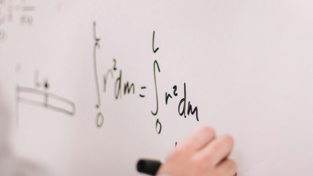 close up of a hand writing a math formula on a white board