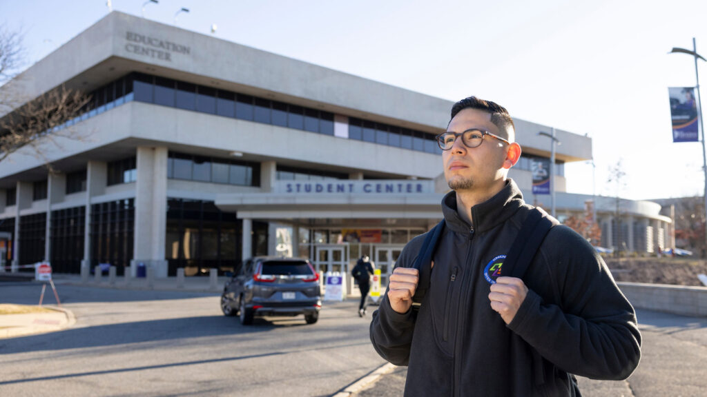 Hispanic college student posing for a portrait outside of a building labeled "Student Center" on a college campus