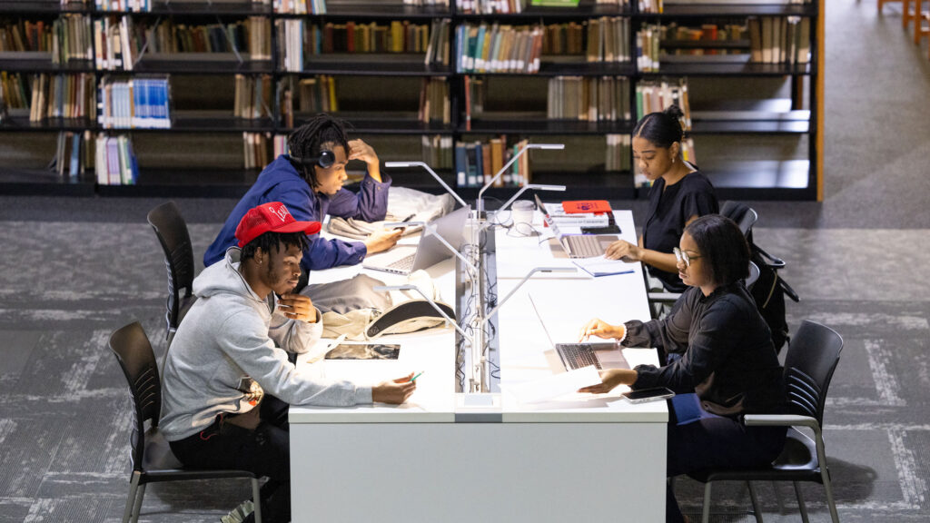 Group of Black college students studying individually at a table at a library