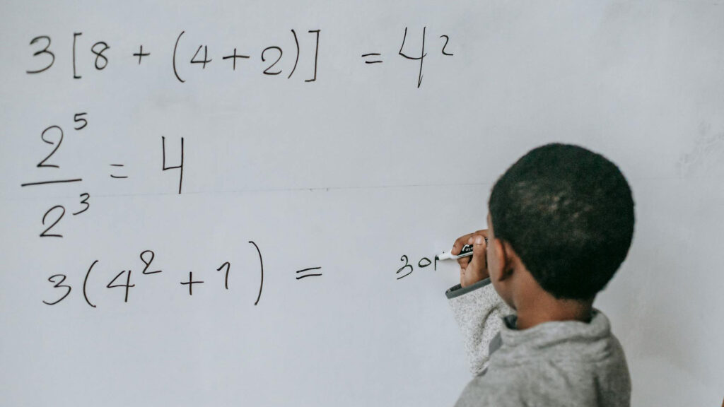 Black male student doing math exercises on a white board