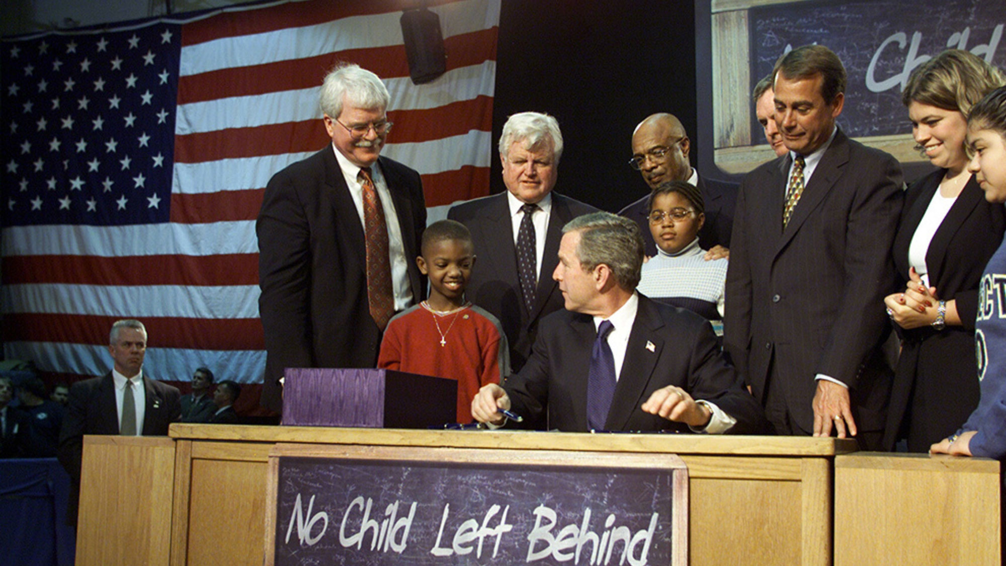 Group photo of President George W. Bush signing the No Child Left Behind Act surrounded by several children and Congressmen