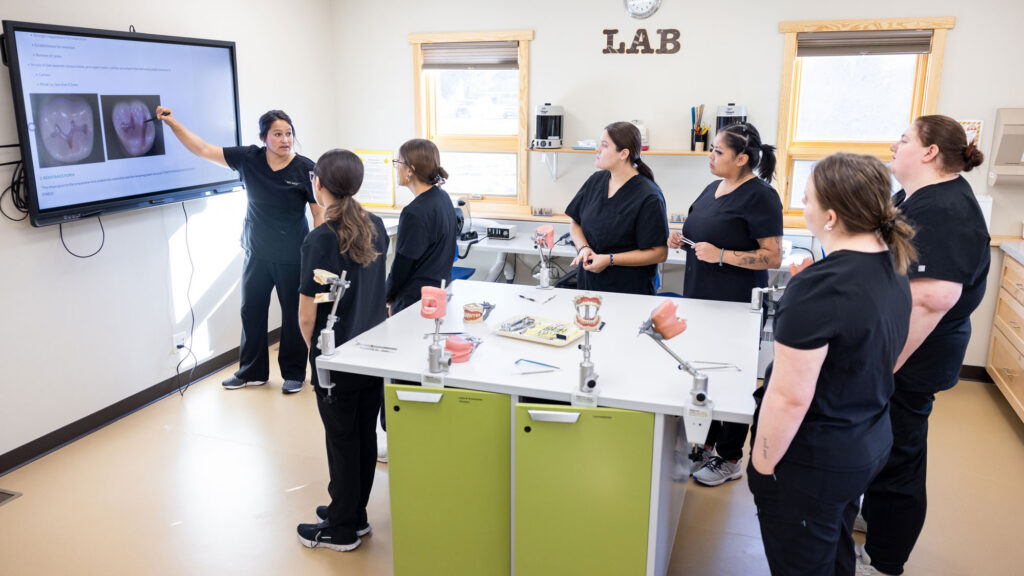 Instructor using a computer display to teach a class in a dental lab on a college campus.