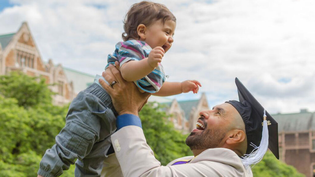 A man wearing a graduation cap holding a toddler up in the air