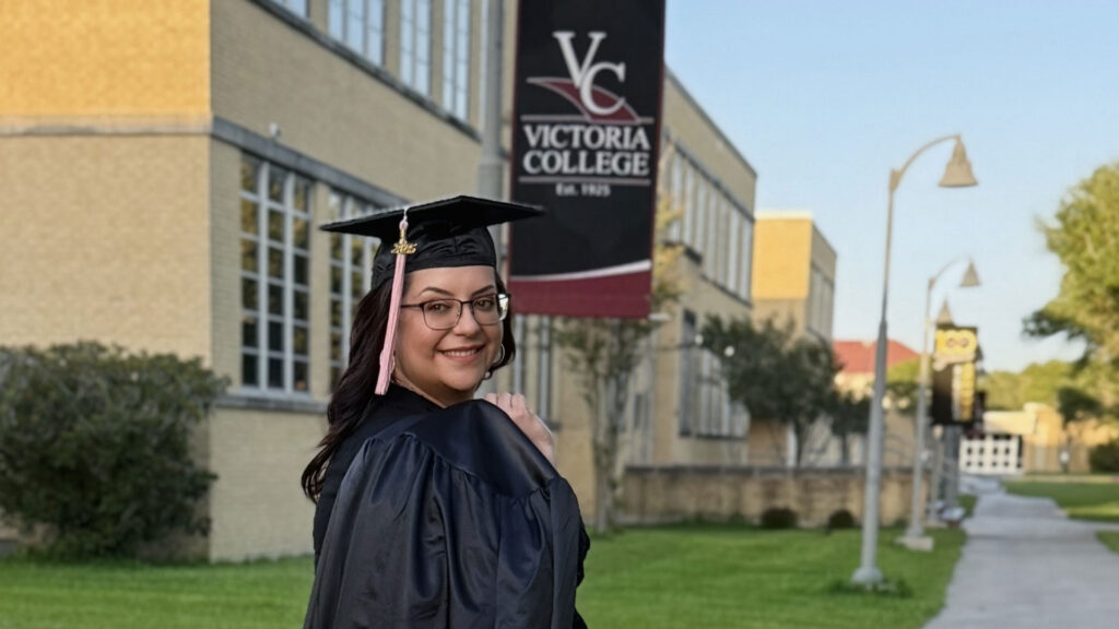 female college graduate in robes and toga posing with Victoria College banner in the background